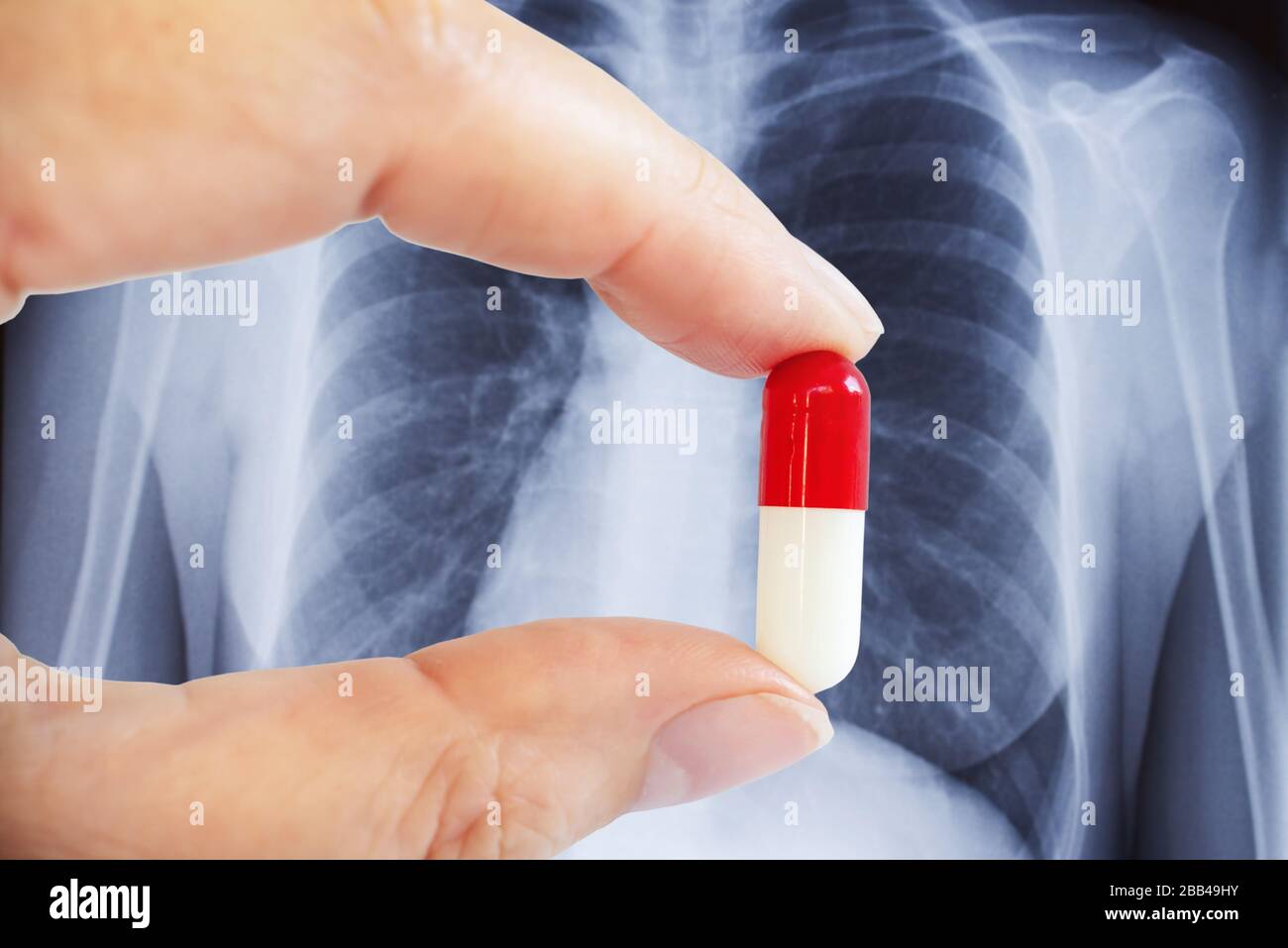 Hand, die eine Tablette, Lunge xray im Hintergrund hält, Coronavirus, Kovid-19-Behandlungskonzept Stockfoto