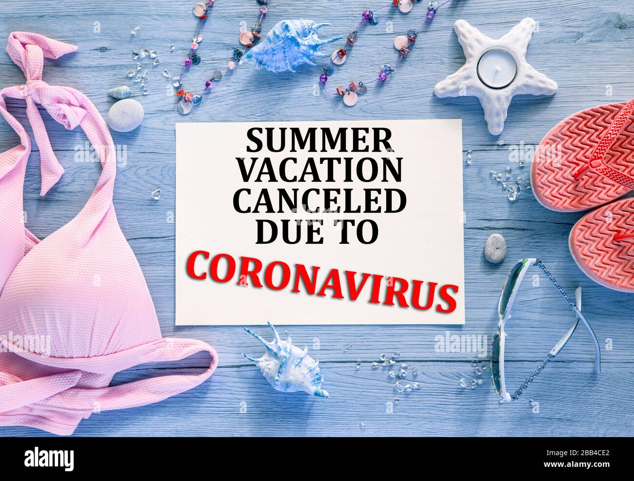 Abstrakter Farbhintergrund mit Text: Sommerurlaub wegen Coronavirus abgesagt. Pinkfarbene Bikini, Korallenflippflops und Sonnenbrille, blauer Holzhintergrund Stockfoto