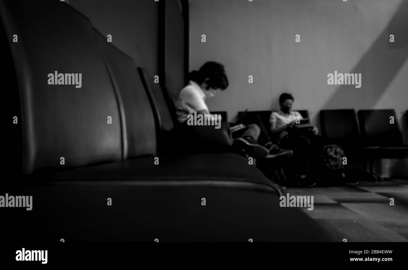Verschwommene Frauen tragen eine chirurgische Maske und sitzen mit einem Laptop auf dem Sitz, um an einem öffentlichen Ort zu arbeiten, der auf Zug- oder Flugflüge wartet. Konzept der sozialen Distanzierung Stockfoto