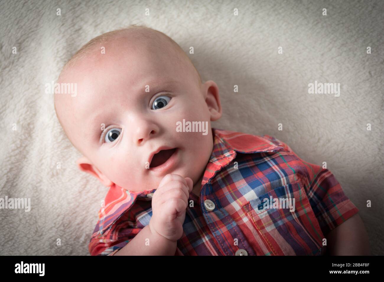 Überraschter Babyjunge mit großen blauen Augen, die direkt auf die Kamera blicken Stockfoto