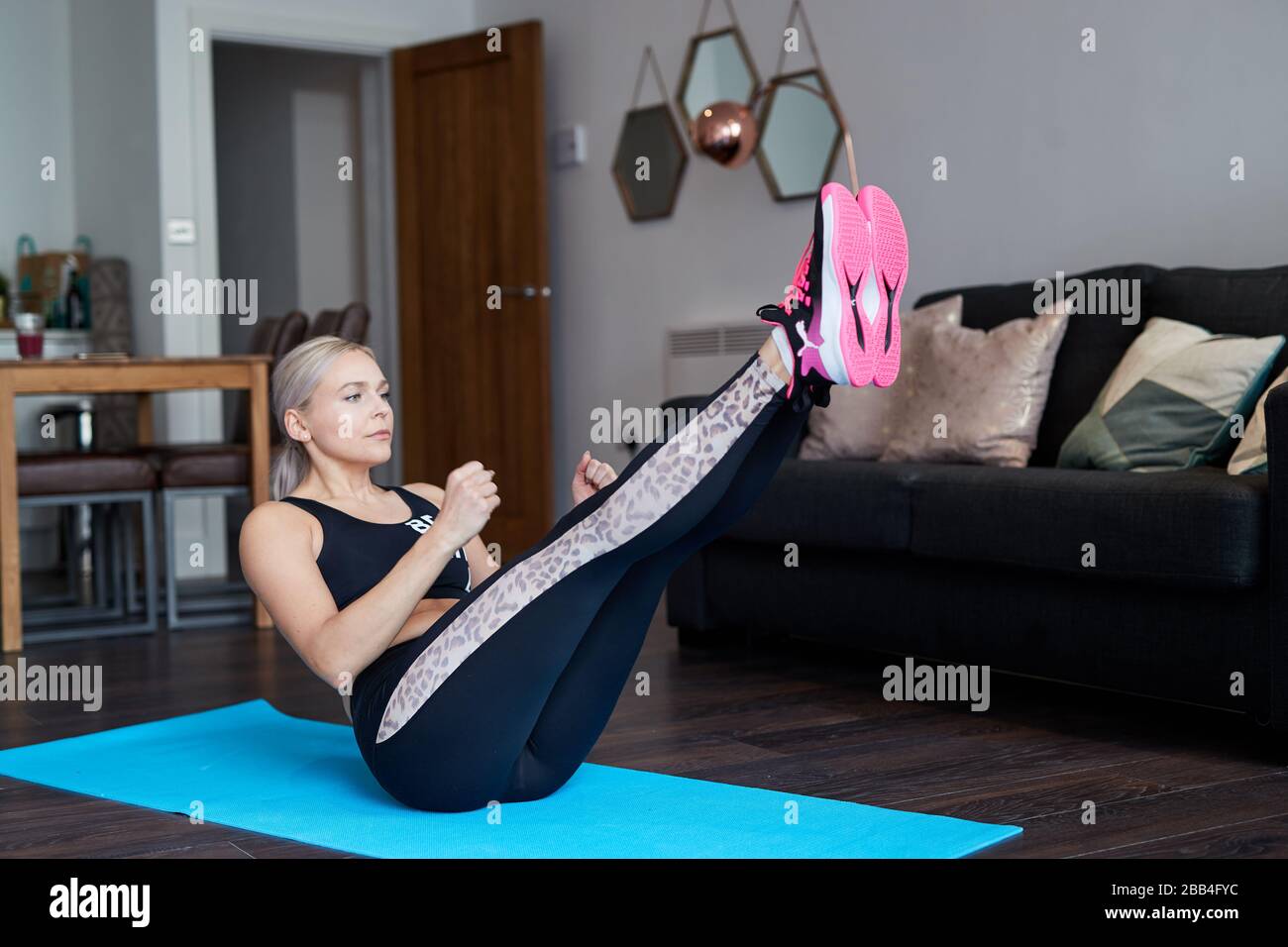 Eine Single Blonde Frau streckt sich, während sie zu Hause auf einer Matte im Wohnzimmer ihrer Wohnung trainiert Stockfoto