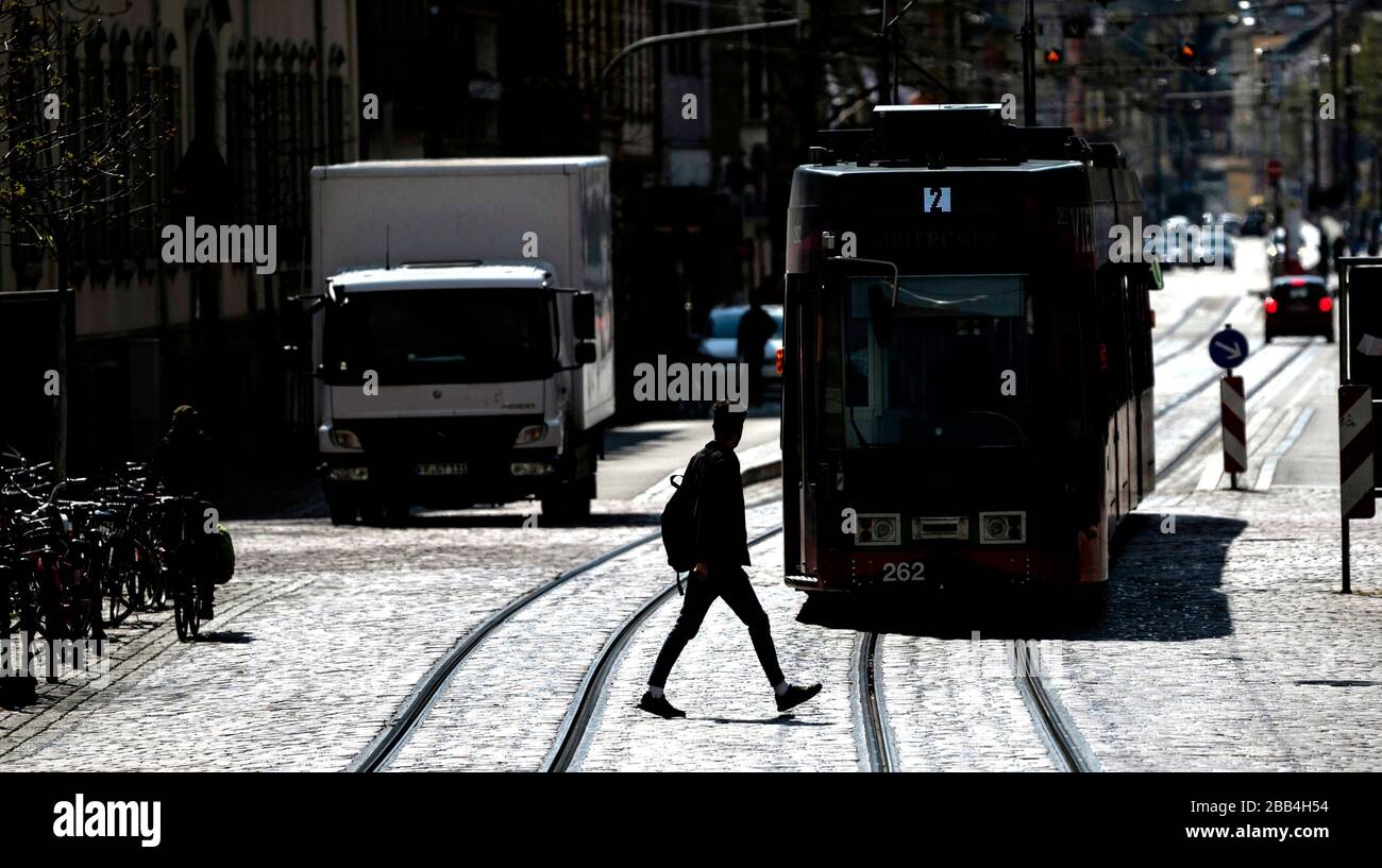 Freiburg, Deutschland. März 2020. Ein Mann läuft hinter einer Straßenbahn. Aufgrund der mit der Corona-Krise verbundenen Ausreisebeschränkungen sind deutlich weniger Menschen unterwegs als sonst, und die Fahrpläne für den öffentlichen Verkehr wurden ausgedünnt. Credit: Patrick Seeger / dpa / Alamy Live News Stockfoto