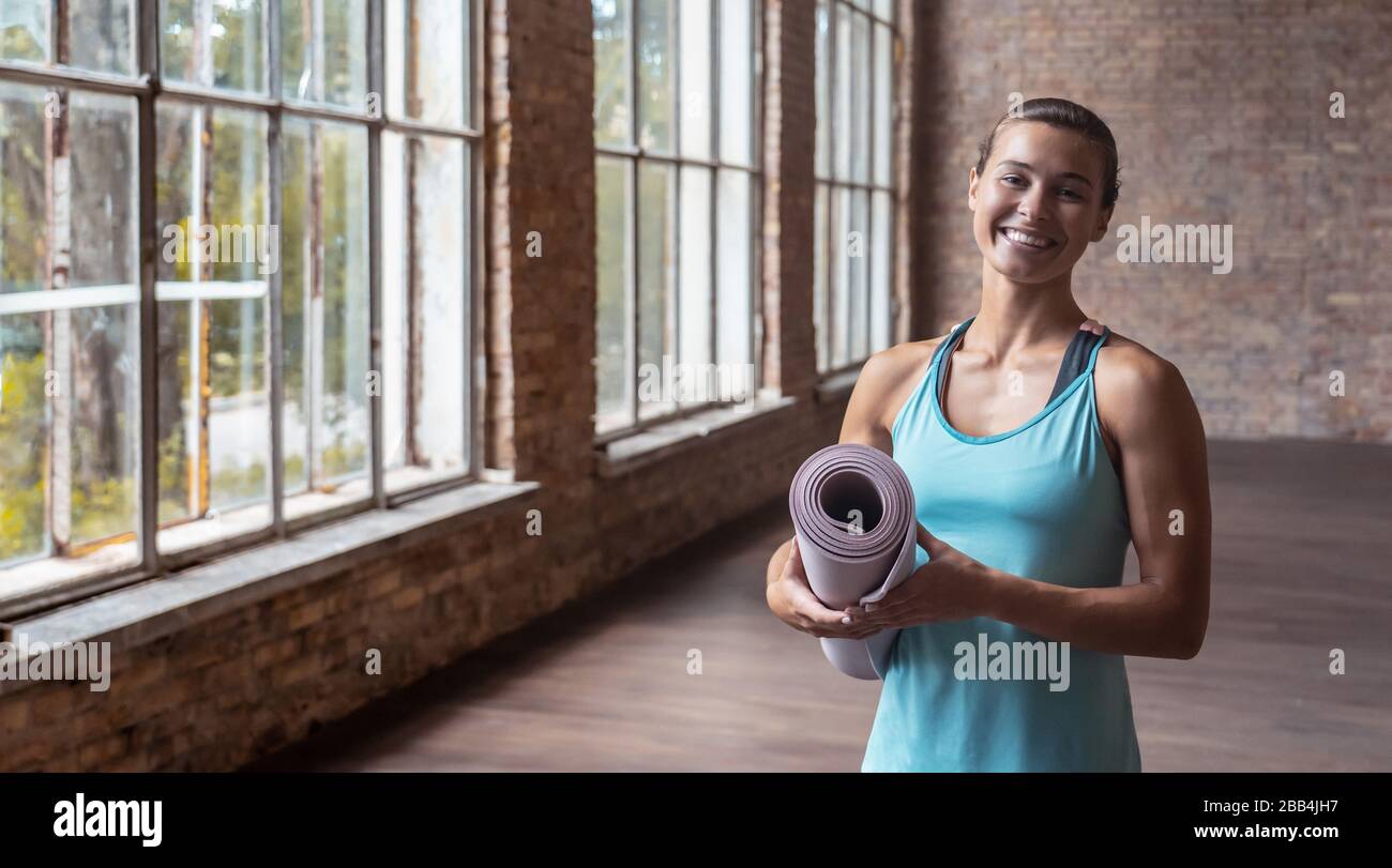 Fröhliche, attraktive junge Frau Yogalehrerin mit Matte und Blick auf die Kamera. Stockfoto