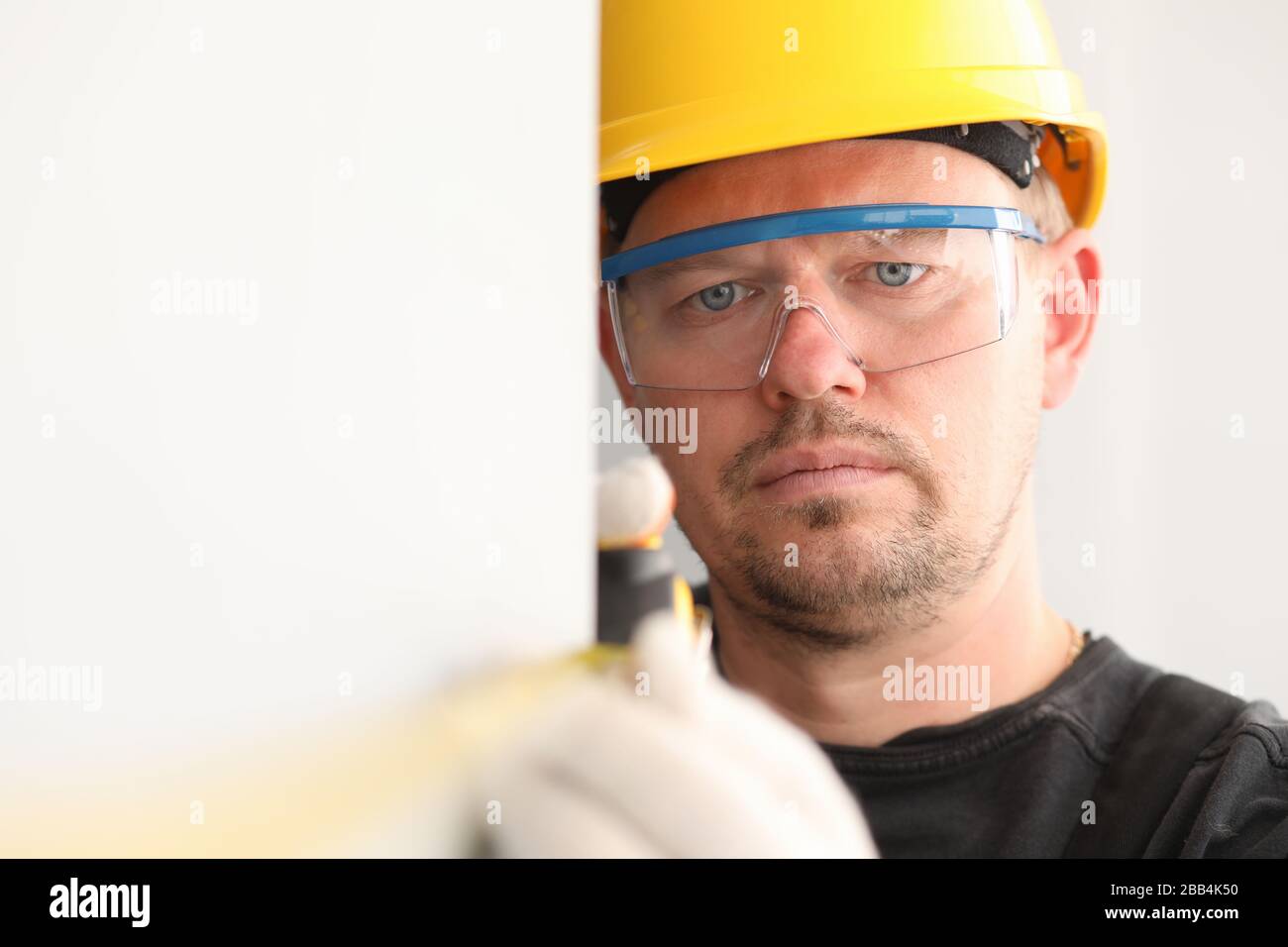 Reparaturmann in Helm und Maske, misst das Maßband Stockfoto