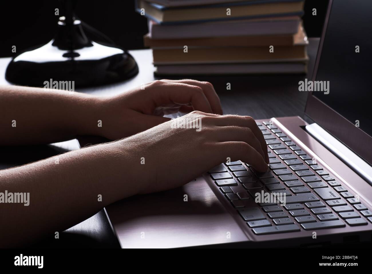 Stillleben in der Nacht unter Lampenlicht. Hände junger Frau, die freiberuflich schreibt, auf der Tastatur des Laptops. Stockfoto