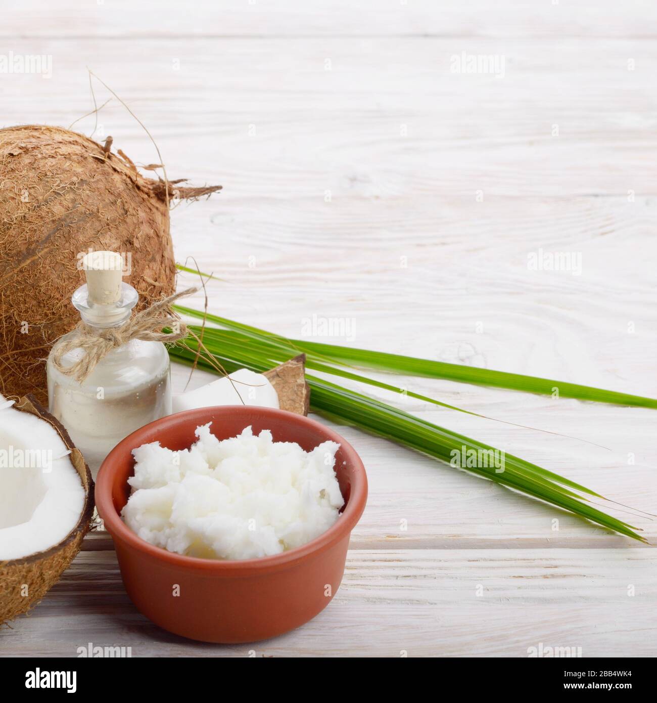 Hintergrund der Kokosnuss, Kokosnussschalen, Öl in Ton Schüssel und Glas auf weissem Holztisch Stockfoto