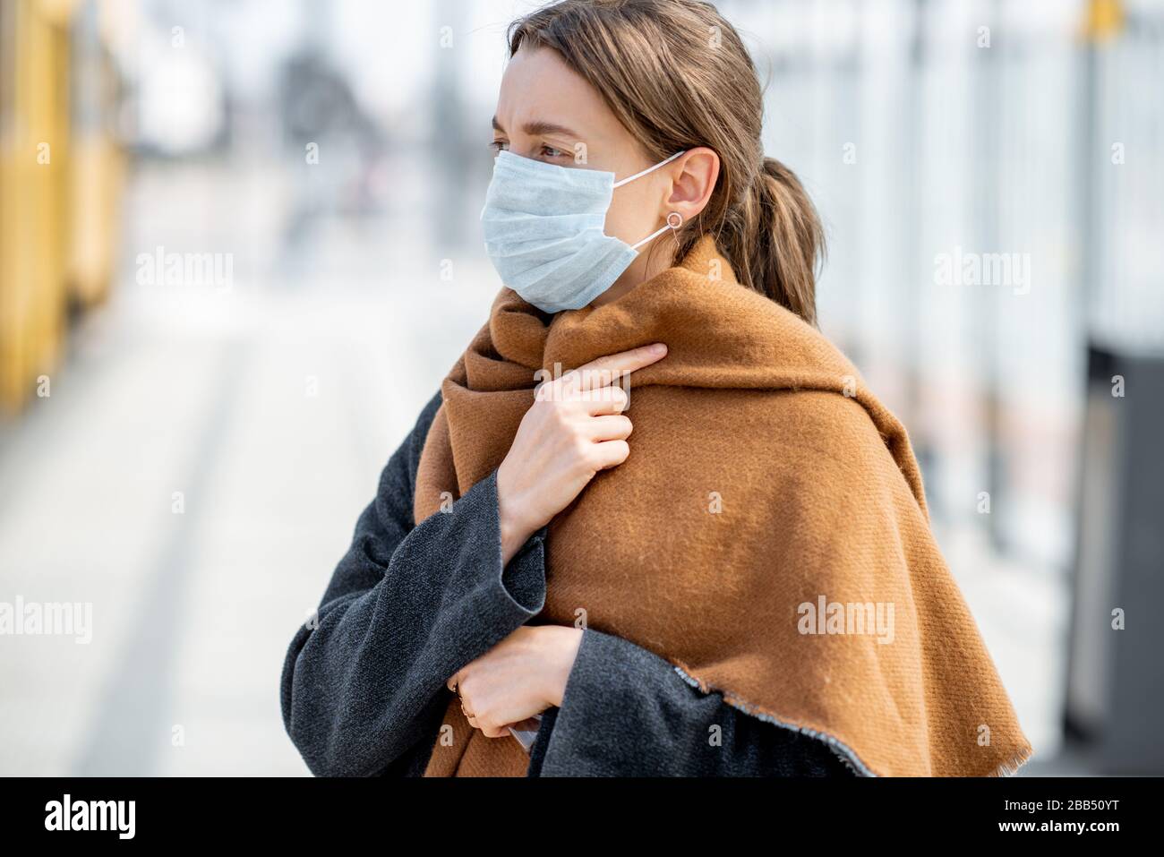 Depressive Frau mit Gesichtsmaske an einem öffentlichen Verkehrshalt im Freien. Konzept der Coronavirus Epidemie, Prävention der Ausbreitung der Infektion oder Schutz vor schlechter Luftverschmutzung Stockfoto
