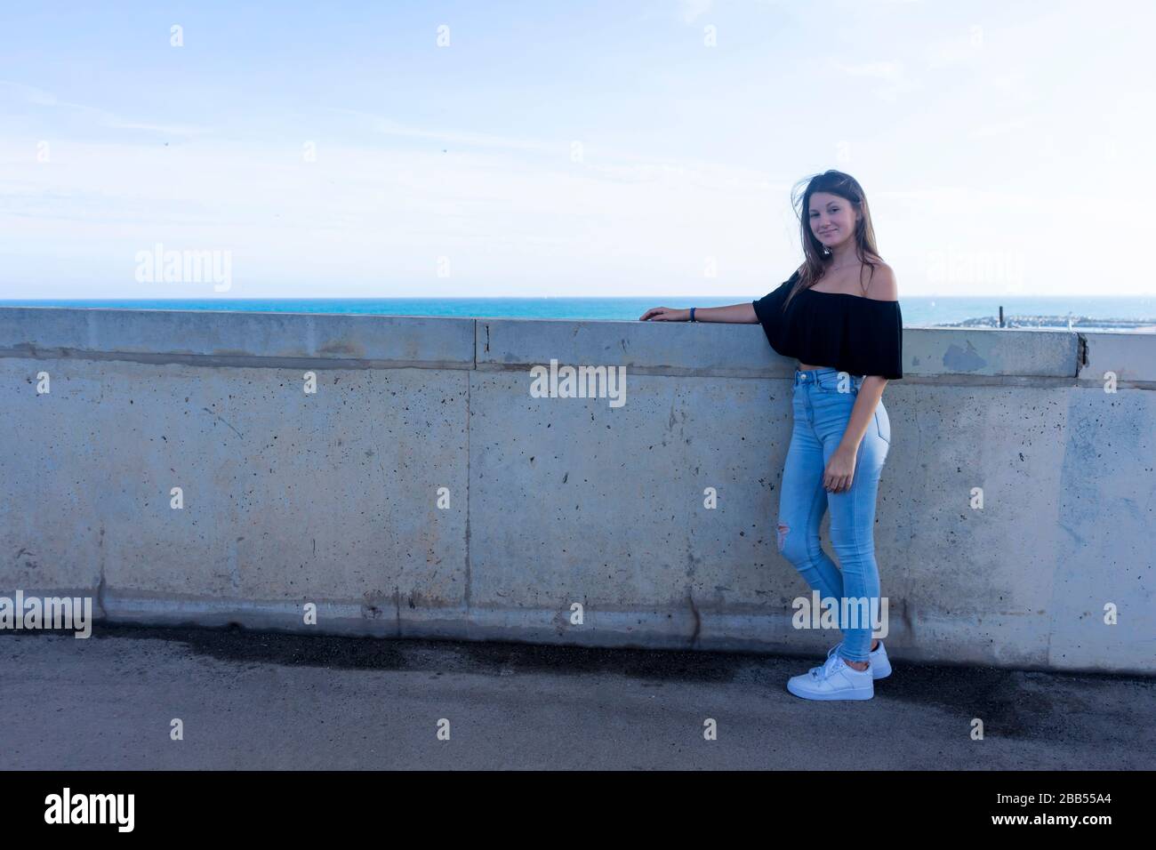 Eine junge, schöne Frau mit langen Haaren, die sich an die Wand der Promenade lehnt und dabei auf die Kamera aufdringlich aussieht Stockfoto