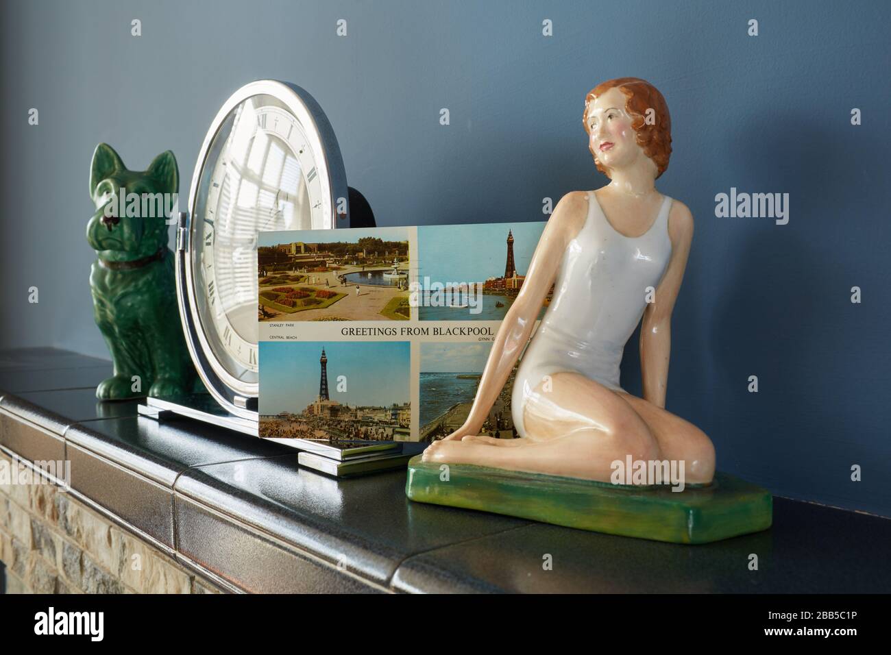 Foto von Gegenständen auf einem Kaminmantelregal aus den 1960er Jahren, einschließlich Kunst-Deko-Uhr, Figur und Postkarte aus Blackpool. Stockfoto