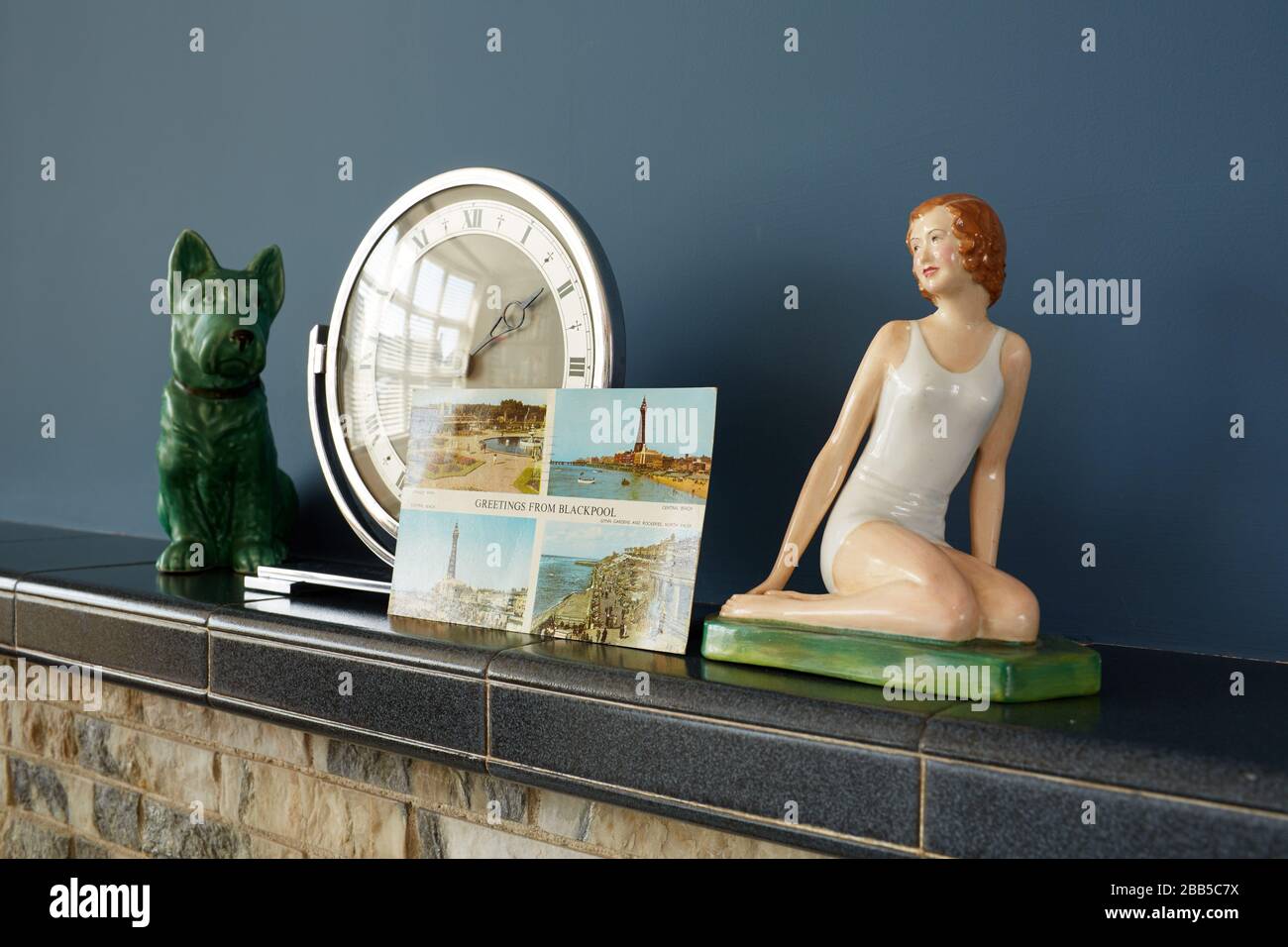 Foto von Gegenständen auf einem Kaminmantelregal aus den 1960er Jahren, einschließlich Kunst-Deko-Uhr, Figur und Postkarte aus Blackpool. Stockfoto