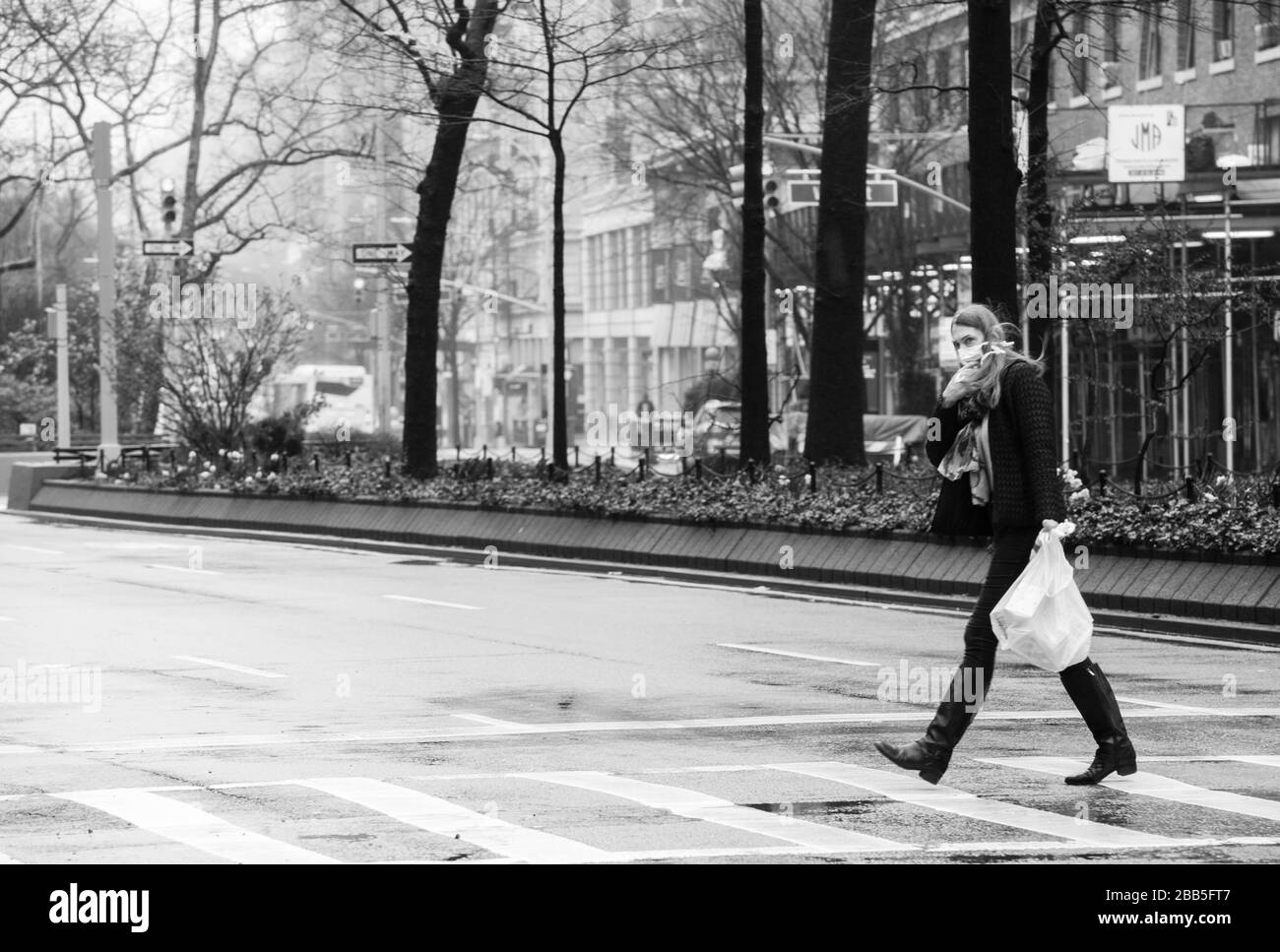Dies ist ein Foto einer gewöhnlichen Frau, die die Straße auf der oberen Westseite der Stadt New York überquert und aufgrund der Bedrohung durch Corona eine chirurgische Maske trägt Stockfoto