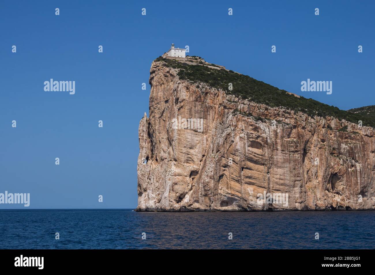 Ruhiges blaues Wasser des Mittelmeeres, umliegende Halbinsel Capo Caccia mit einem weißen Gebäude auf der Spitze der Klippe. Strahlend blauer Himmel. Sardinien, Ital Stockfoto