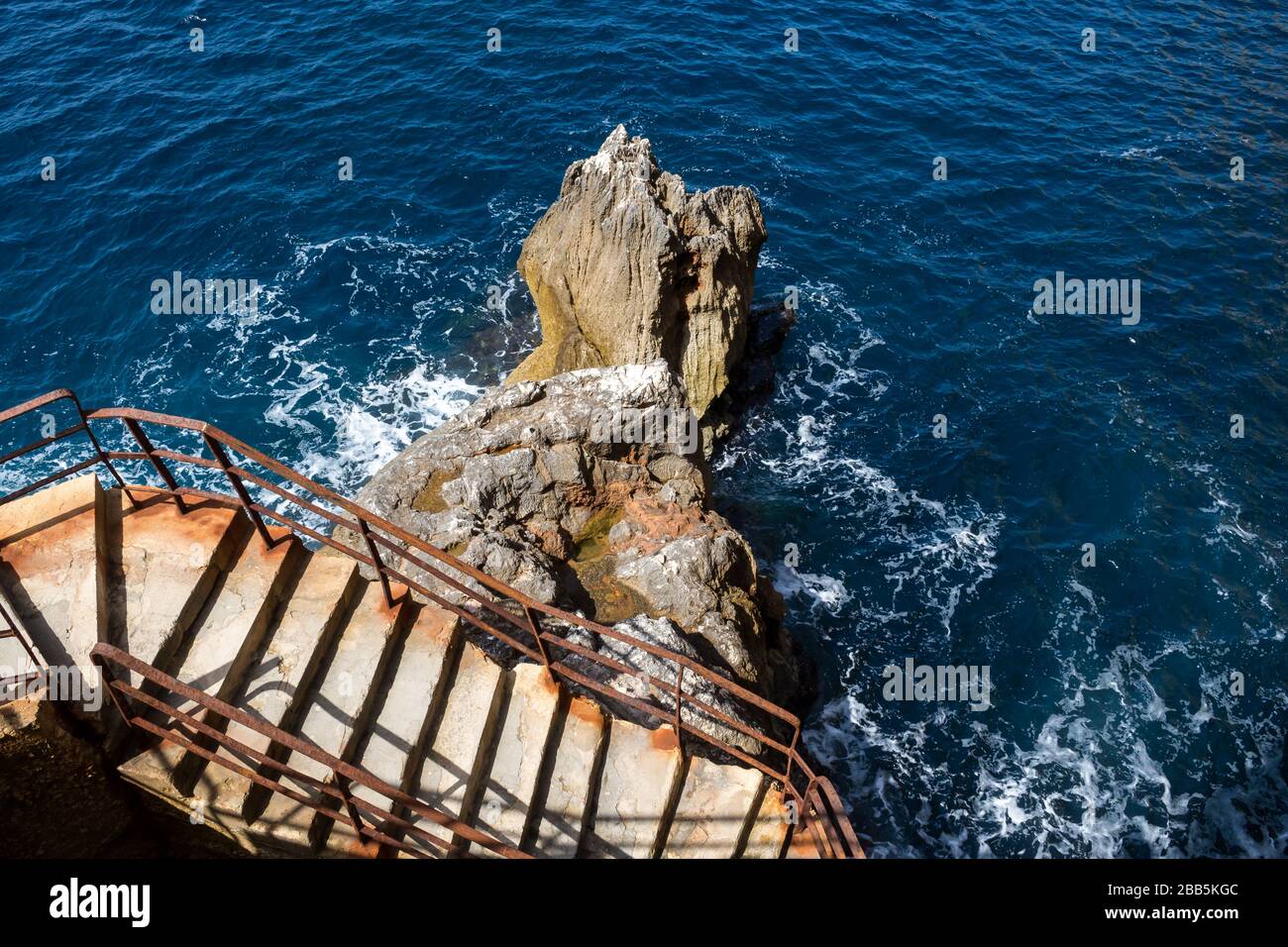 Alte Betontreppen, die eine Klippe mit einem verrosteten Handlauf sägen. Felsen im Mittelmeer neben. Grotta di Nettuno, Insel Sardinien, Italien. Stockfoto