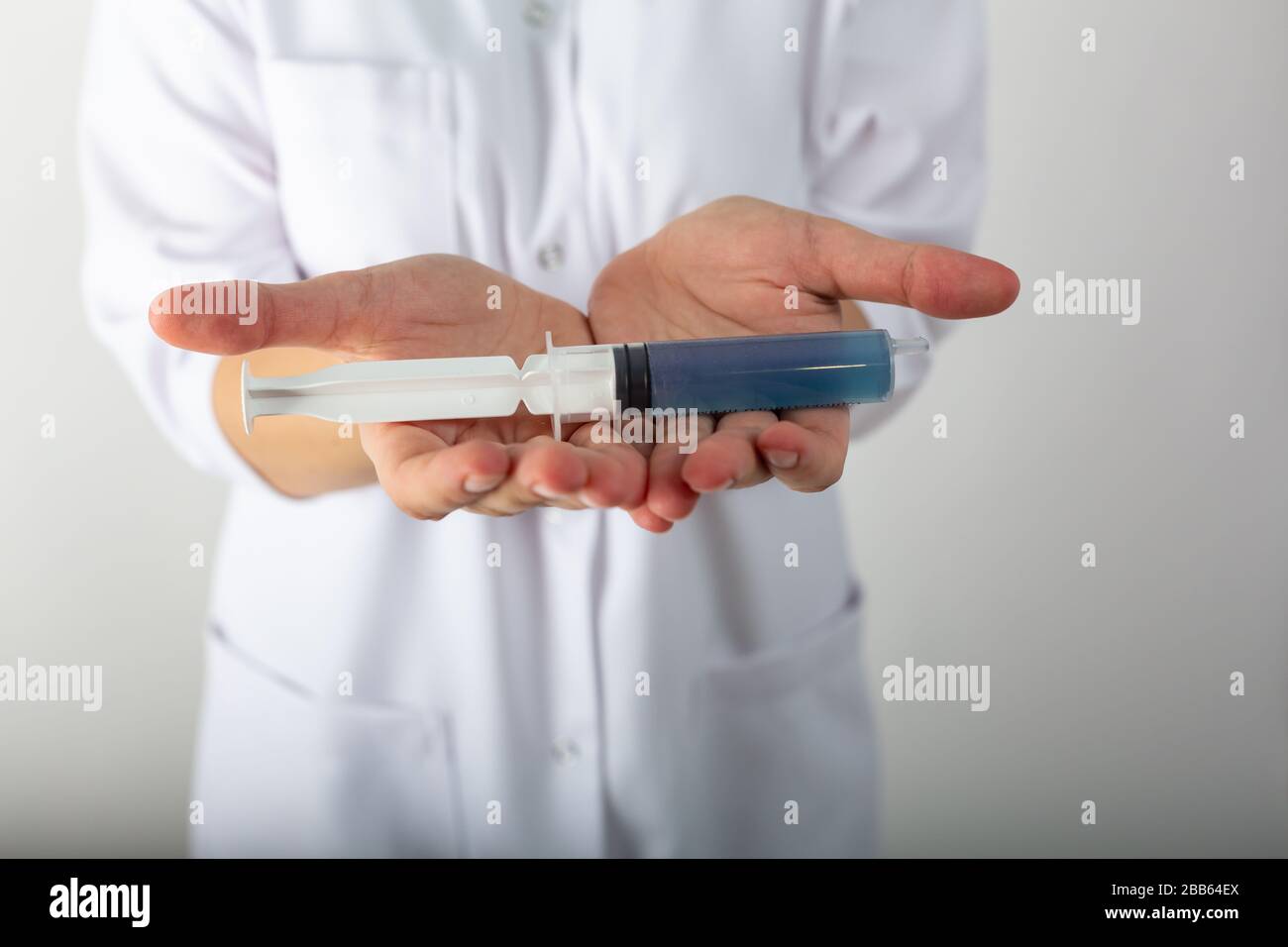 Mädchen in einem medizinischen Mantel hält eine große Spritze mit blauer Flüssigkeit - Coronaviris-Impfstoff Stockfoto