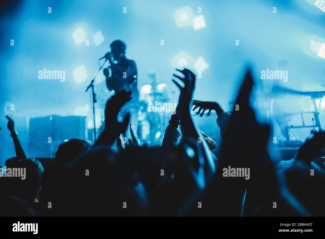 Konzertsilhouetten bei einem Konzert sind Menschen sichtbar, von Bühnenleuchten hinterleuchtet, erhöhte Hände. Stockfoto