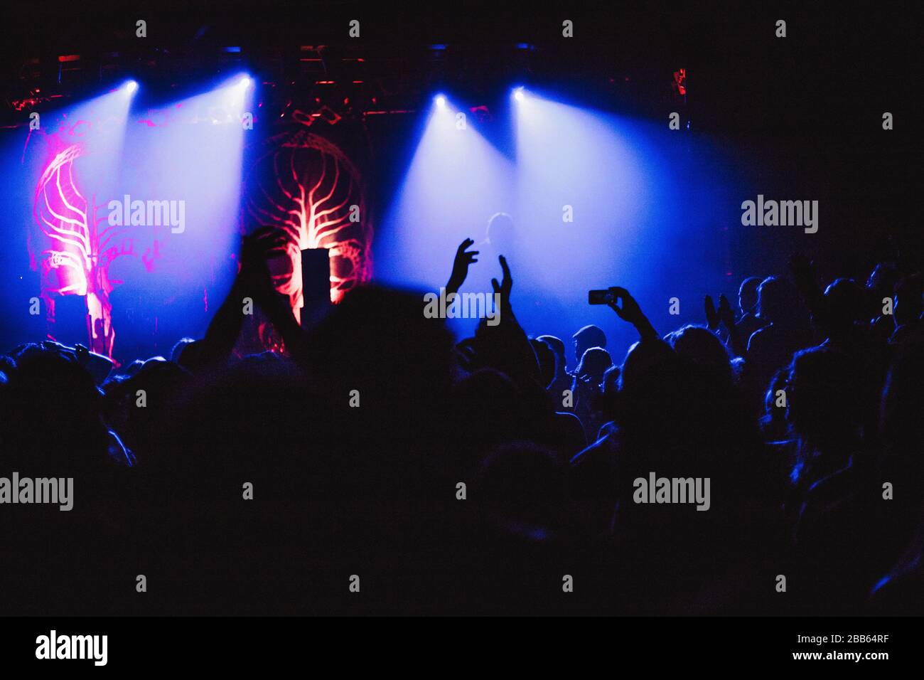 Konzertpublikum bei einem Konzert sind die Silhouetten der Menschen sichtbar, die durch Bühnenbeleuchtung, erhöhte Hände und Smartphones beleuchtet werden. Stockfoto