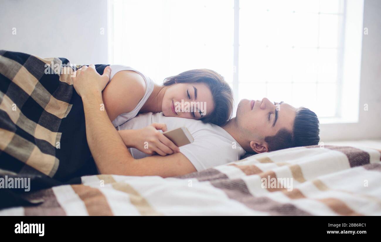 Auf dem Bett liegt ein liebevolles Paar. Eine Frau verwendet ein Smartphone. Stockfoto
