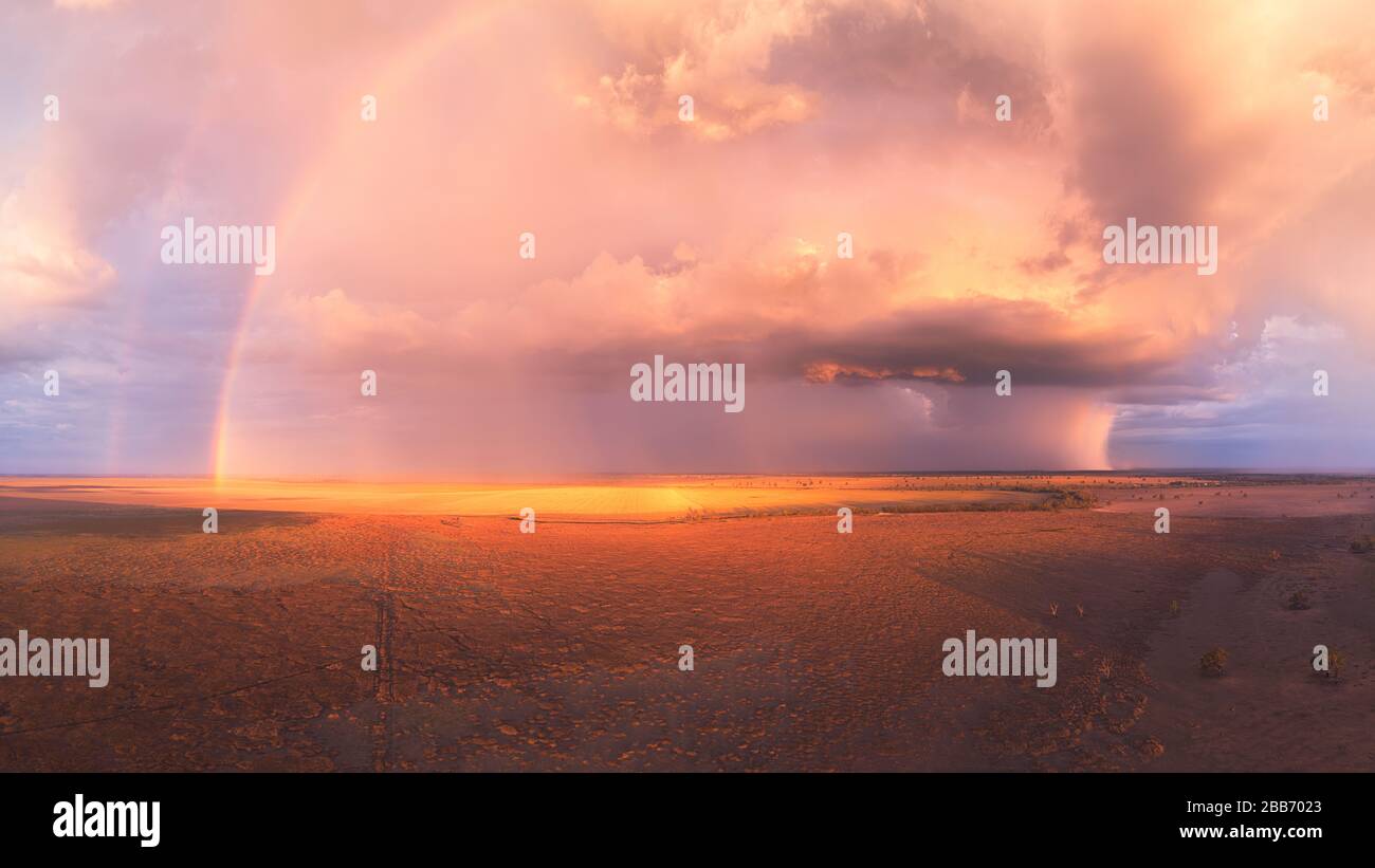 Stürmischer Sonnenuntergang mit doppeltem Regenbogen, hoch aufragender cumulus-wolke und Regenzellen über einem trockenen See in Australien Stockfoto