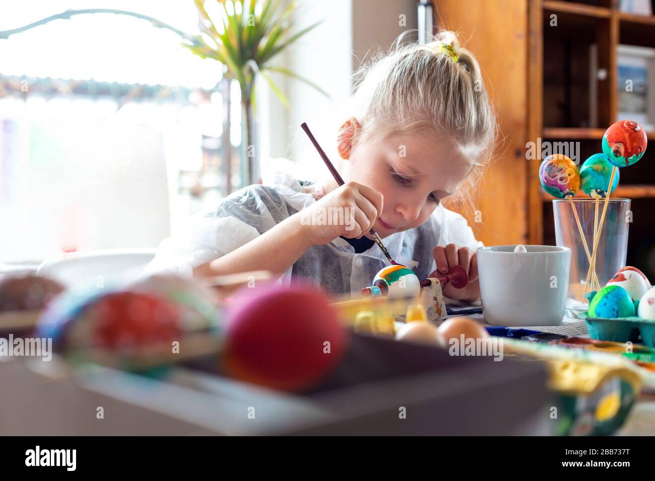 Porträt eines liebenswerten blonden Mädchens zu Hause, das Ostereier malt Stockfoto