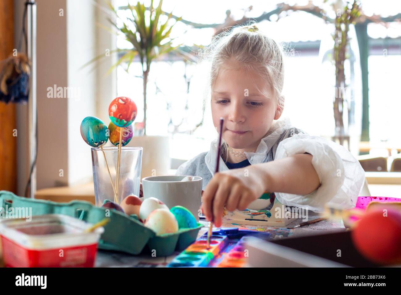 Porträt eines liebenswerten blonden Mädchens zu Hause, das Ostereier malt Stockfoto