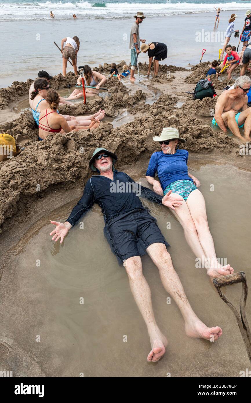 Touristen, die sich in heißen Pools entspannen, die im Sand gegraben wurden, Hot Water Beach, in der Nähe von Hahei, North Island, Neuseeland Stockfoto