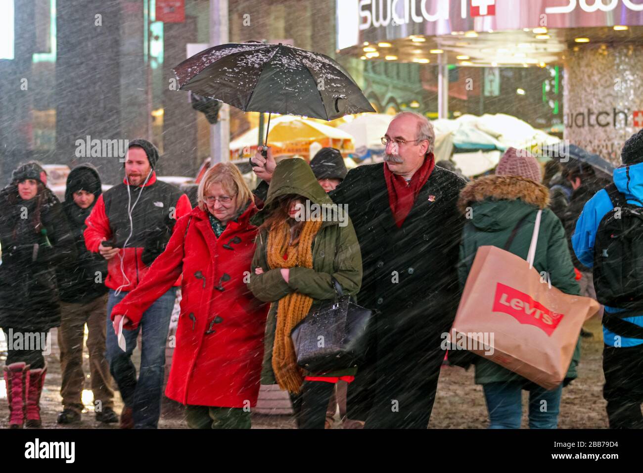 Älterer Herr, der seine Frau und seine Tochter während eines schneesturms auf dem Time Square, Manhattan, New York City, Vereinigte Staaten mit Regenschirm bedeckt Stockfoto
