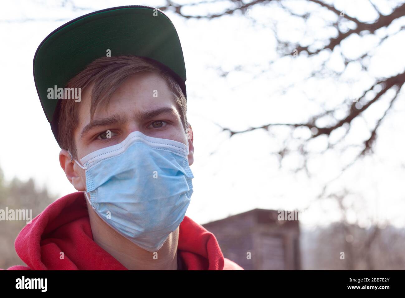 Rot gekleideter Kerl steht in einer medizinischen Maske in der Nähe auf der Straße und verhindert die Verbreitung des Virus-Kovid-19, Gesundheitskonzept. Stockfoto