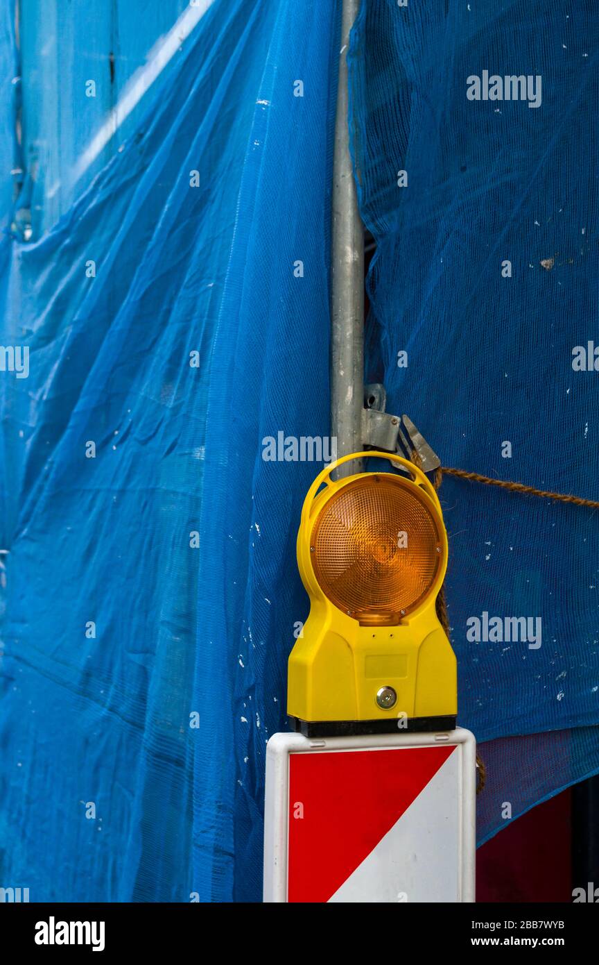 Warnleuchte am Backen vor einer Baustelle. Hausrenovierung. Die Renovierung wurde mit blauem Stoff unterbrochen Stockfoto