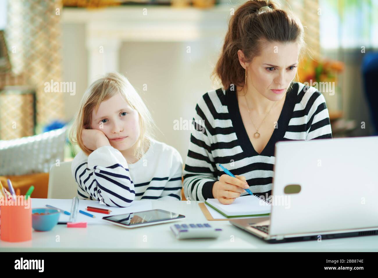 Langweilige Kinder erwecken Aufmerksamkeit, während die Mutter im Büro im modernen Wohnzimmer an sonnigen Tagen arbeitet. Stockfoto