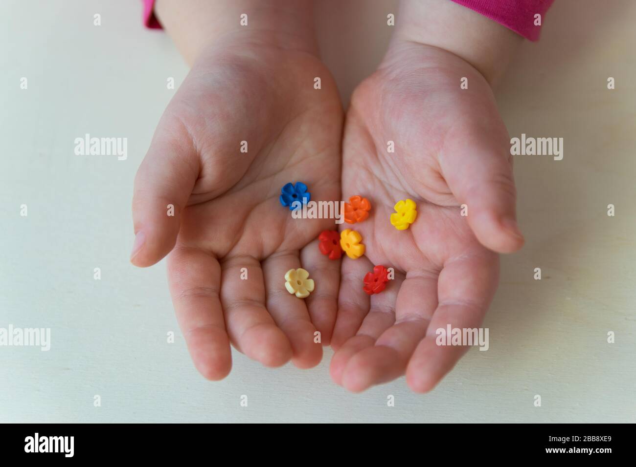 Hände des Kindes, das die kleinen Spielzeuge auf dem Holzhintergrund hält. Bunte Plastikblumen in den Kinderhänden. Stockfoto