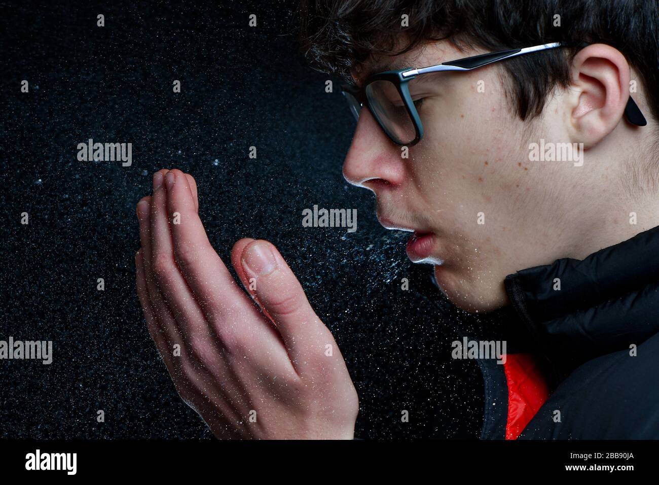 Ein Teenager-Junge, der niest/hustet, zeigt die Menge an Spray oder Virus, die aus dem Mund kommt. Konzeptbild, um zu zeigen, wie sich Bakterien ausbreiten. Stockfoto