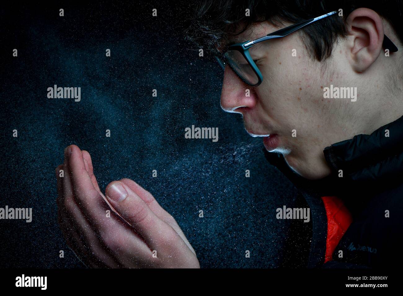 Ein Teenager-Junge, der niest/hustet, zeigt die Menge an Spray oder Virus, die aus dem Mund kommt. Konzeptbild, um zu zeigen, wie sich Bakterien ausbreiten. Stockfoto