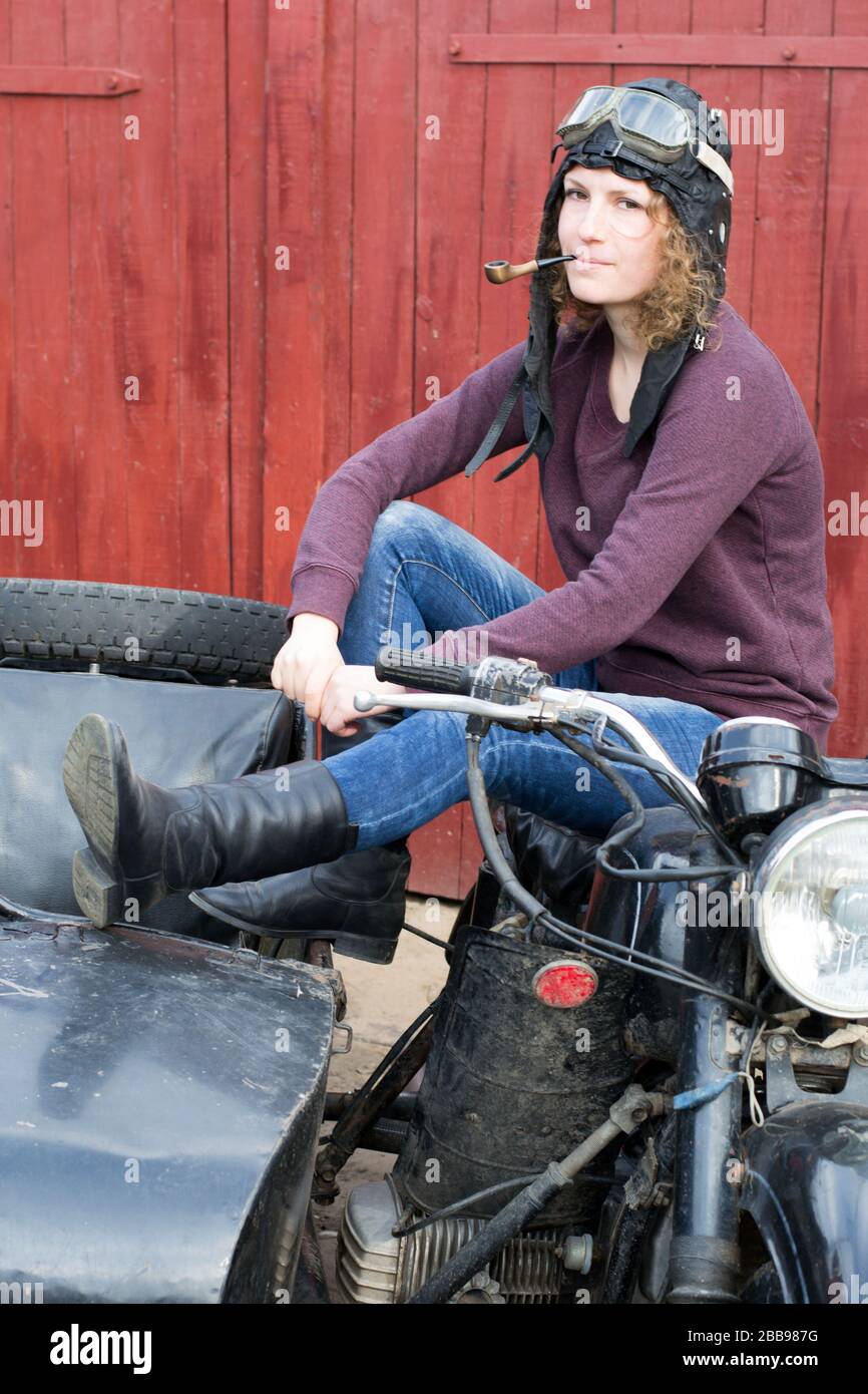 Foto des Mädchens auf Oldtimer Motorrad in Pilotkappe mit Rauchrohr Stockfoto