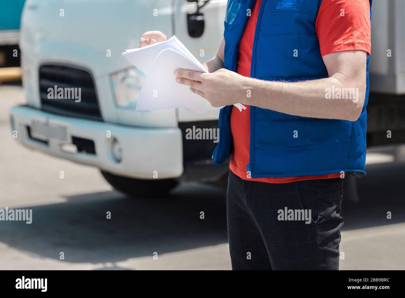 Kurierfahrer in Uniform macht Notizen in Dokument und Lieferung weißer LKW behinde ihn Stockfoto