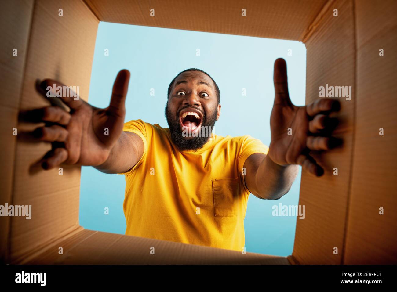 Der glückliche Junge erhält ein Paket aus dem Online-Shop. Glücklicher und überraschter Ausdruck. Blauer Hintergrund Stockfoto