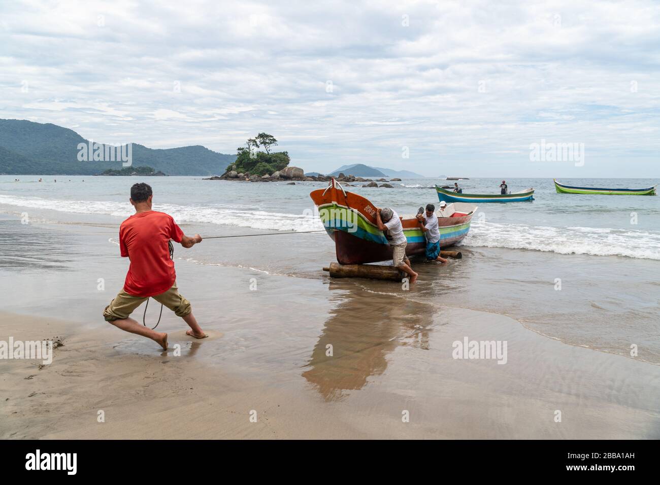 Fischer ziehen ein Holzkanu aus dem Wasser, in Ilhabela, Brasilien. Caiçara Stockfoto