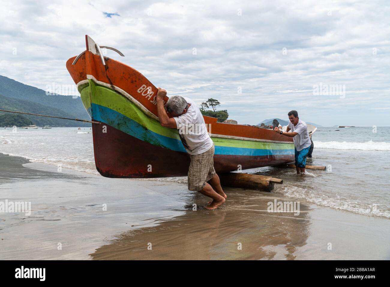 Fischer ziehen ein Holzkanu aus dem Wasser, in Ilhabela, Brasilien. Caiçara Stockfoto