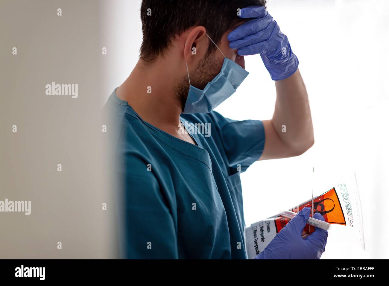 Müder Arzt mit Maske auf hellem Hintergrund, hält Tests in seinen Händen. Epidemischer Ausbruch Stockfoto