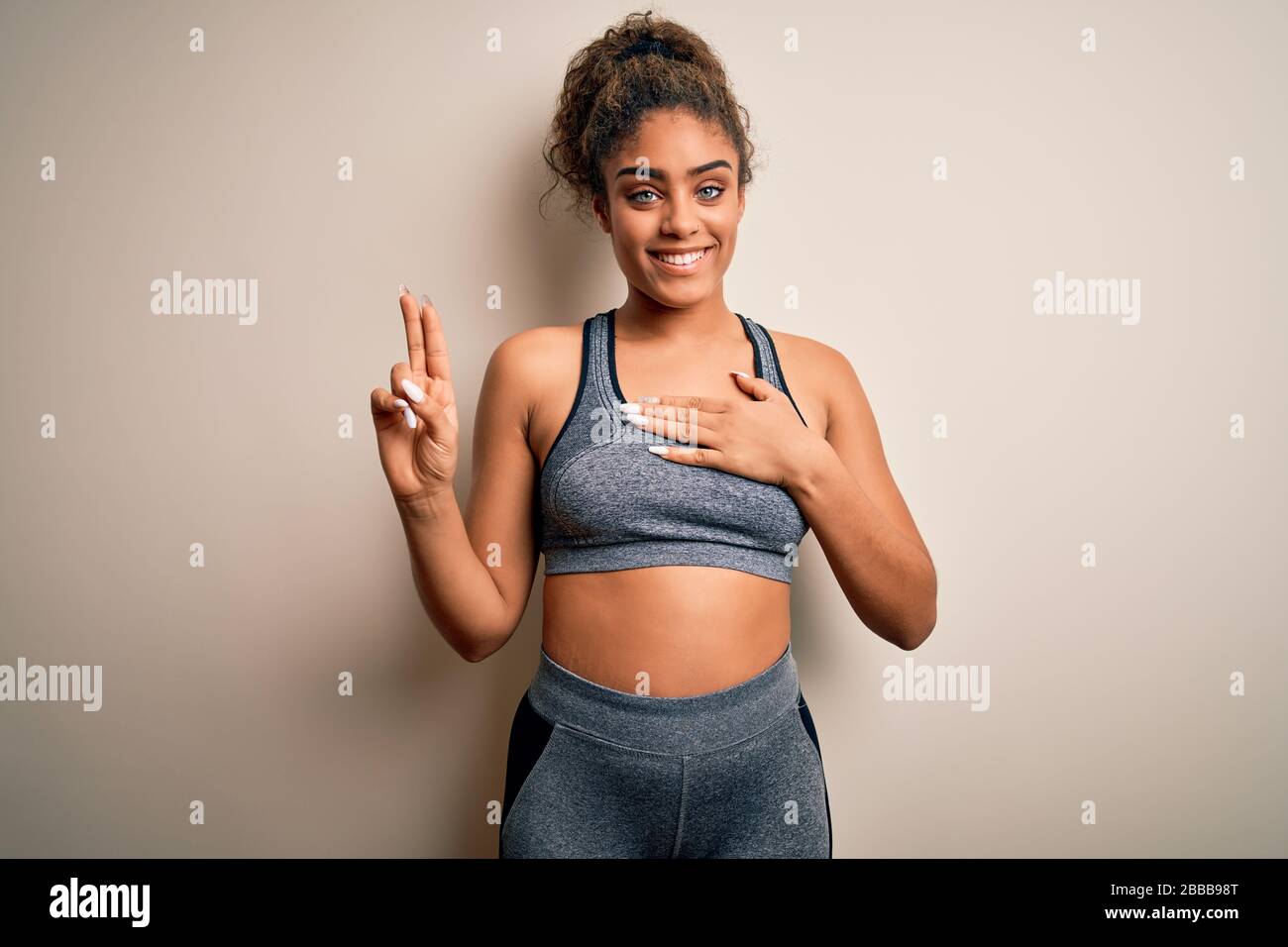 Die junge afroamerikanische Sportlerin, die Sport macht und Sportswear über weißem Hintergrund trägt, lächelt mit der Hand auf der Brust und den Fingern nach oben, was ein l macht Stockfoto