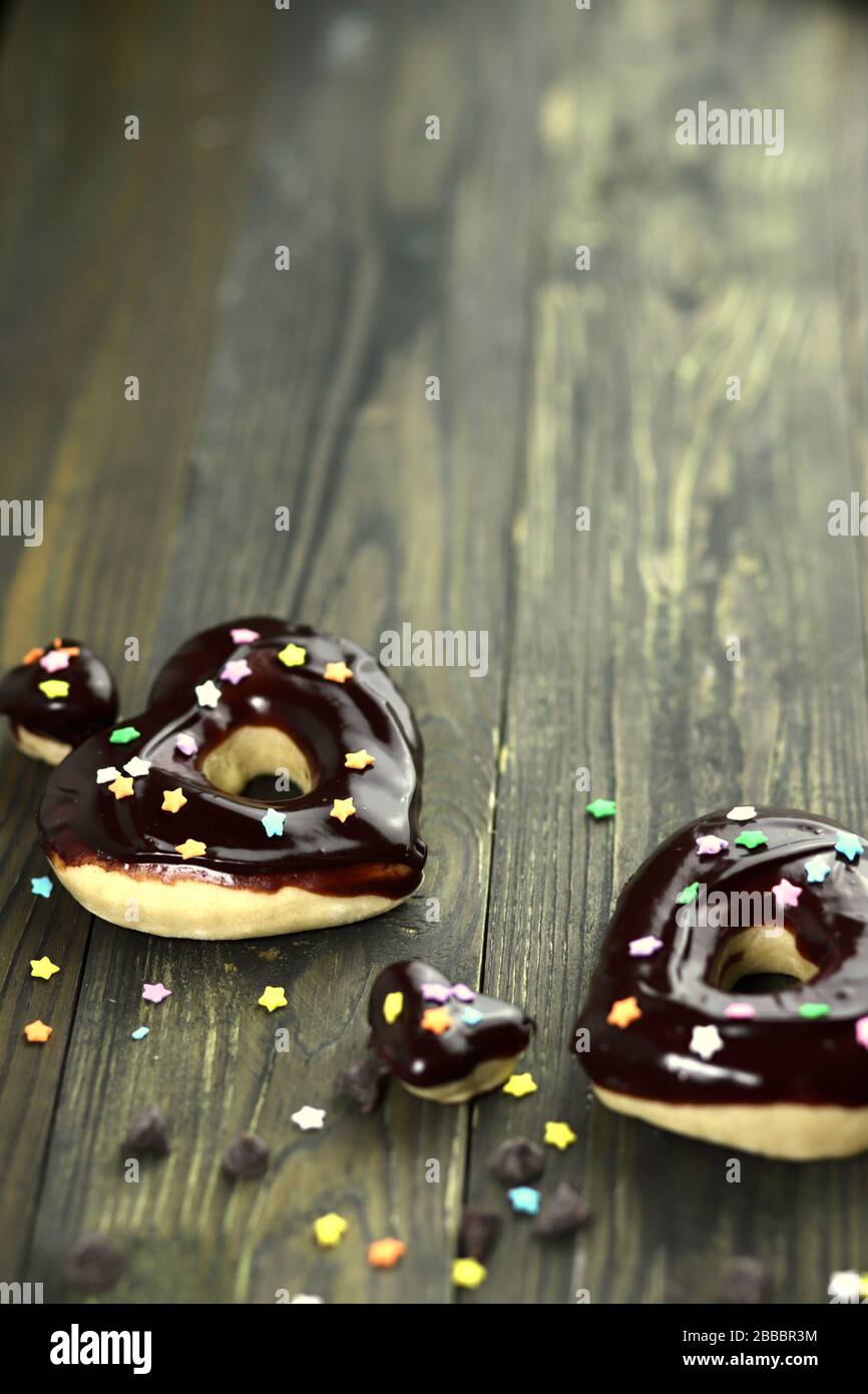 Donuts mit Schokoladenglasur, herzförmige Donut mit Schokoladenglasur, Donuts und Schokoladenchips, Holztisch, Stockfoto