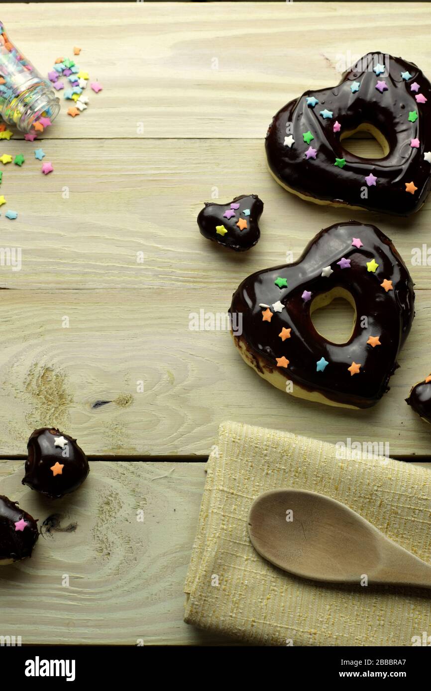 Donuts mit Schokoladenglasur, herzförmige Donut mit Schokoladenglasur, Donuts und Schokoladenchips, Holztisch, Stockfoto
