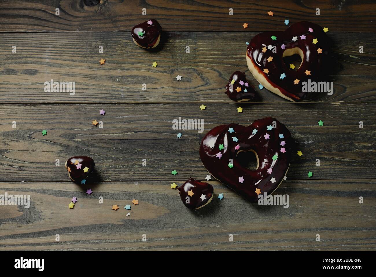 Donuts mit Schokoladenglasur, herzförmige Donut mit Schokoladenglasur, Donuts und Schokoladenchips, Holztisch, Stockfoto