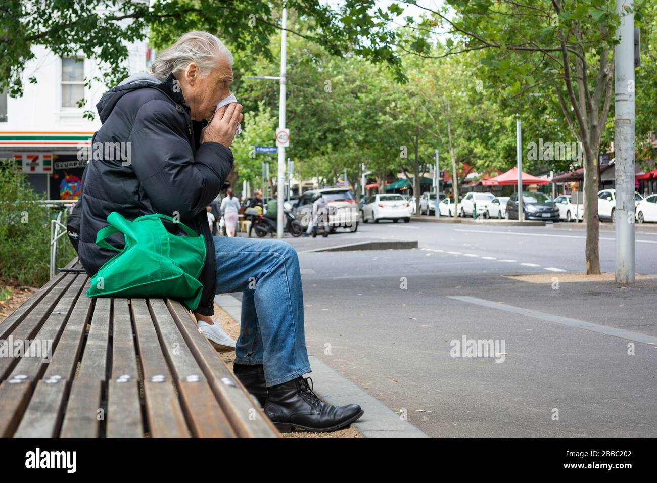 Mann sitzt auf einer Parkbank und weht mit der Nase Stockfoto