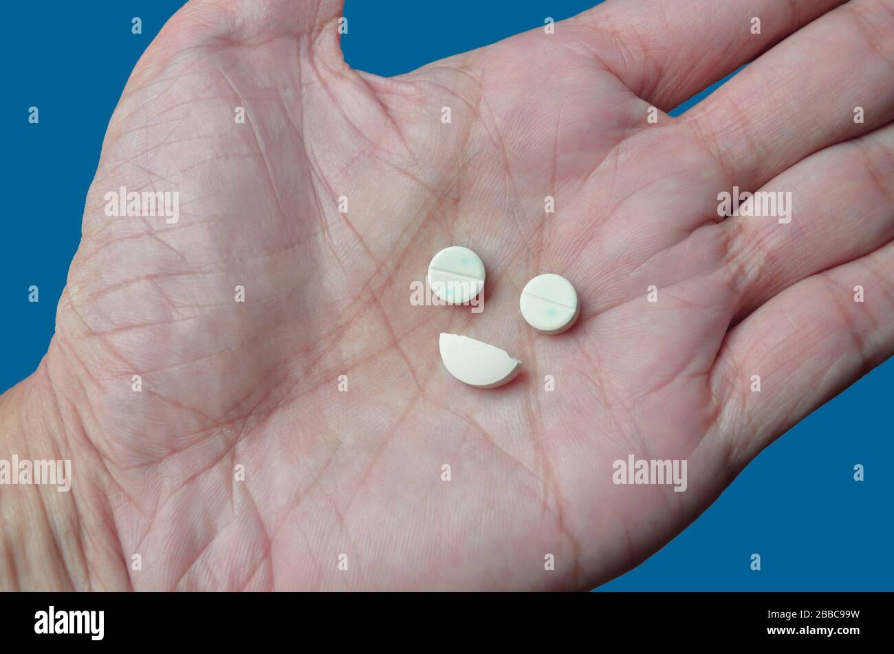 Drogenabhängigkeit, illustriert durch Pillen, die einem glücklichen Gesicht ähneln und je nach Medikament dazu führen, sich gut zu fühlen. Blauer Hintergrund = blaues Gefühl Stockfoto