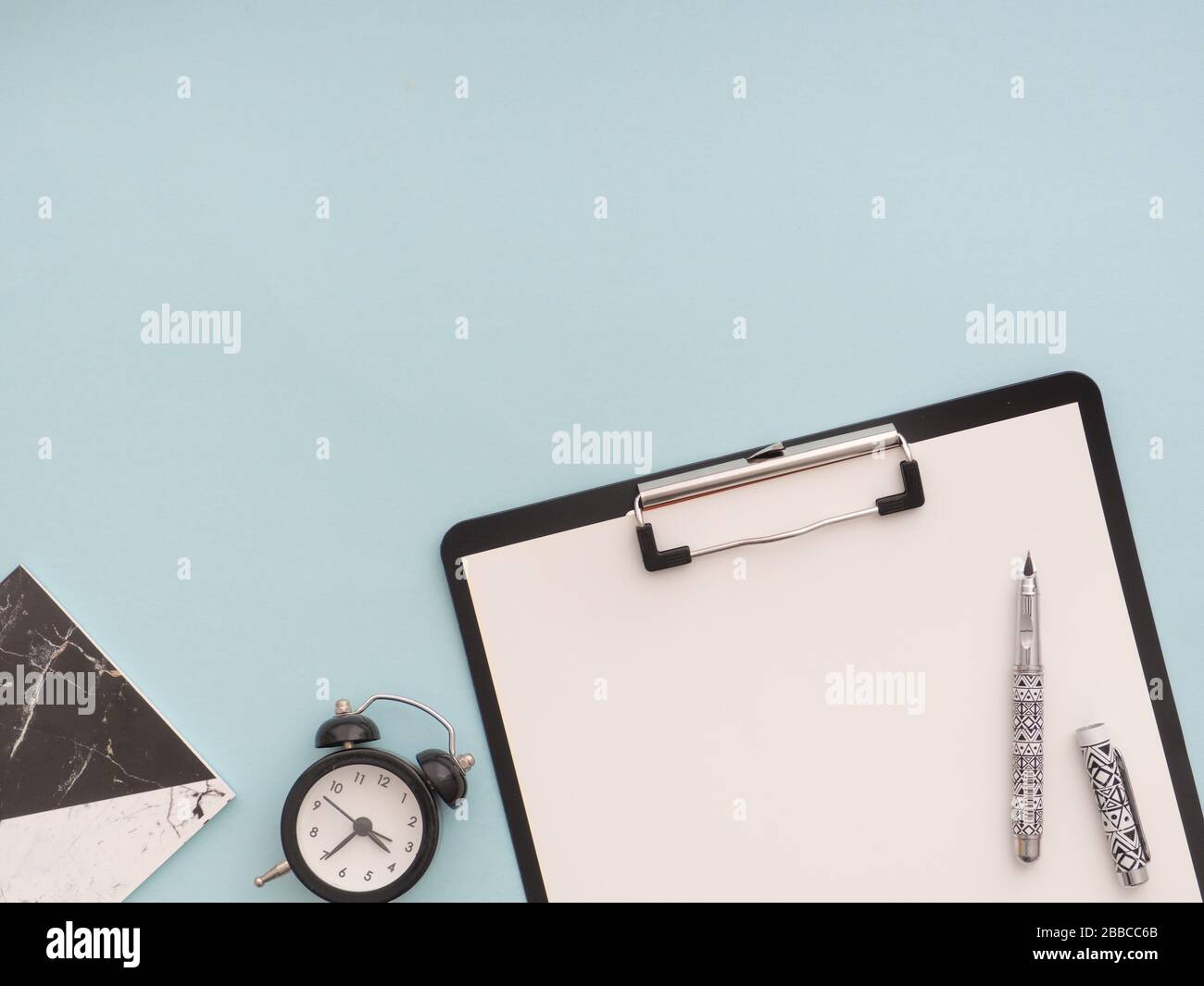 Bürobedarf der Schule, zurück zum Schulkonzept. Schwarze Zwischenablage mit weißem leerem Papier mit Stift darauf, schwarzem Wecker, Schwarz-Weiß-Nein Stockfoto