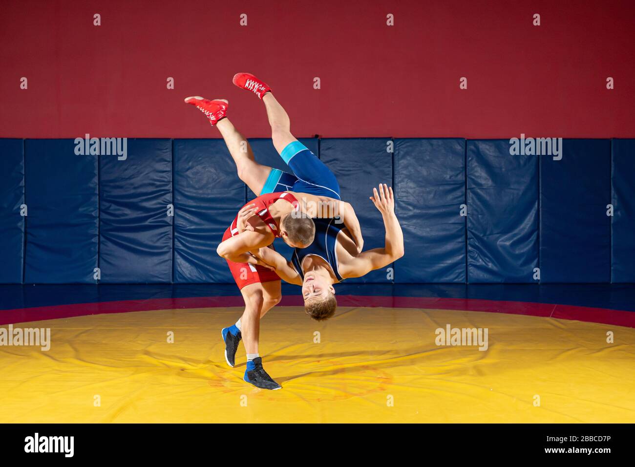 Zwei griechisch-römischen Ringkämpfern in roten und blauen Uniform wrestling auf einem gelben wrestling Teppich in der Turnhalle Stockfoto