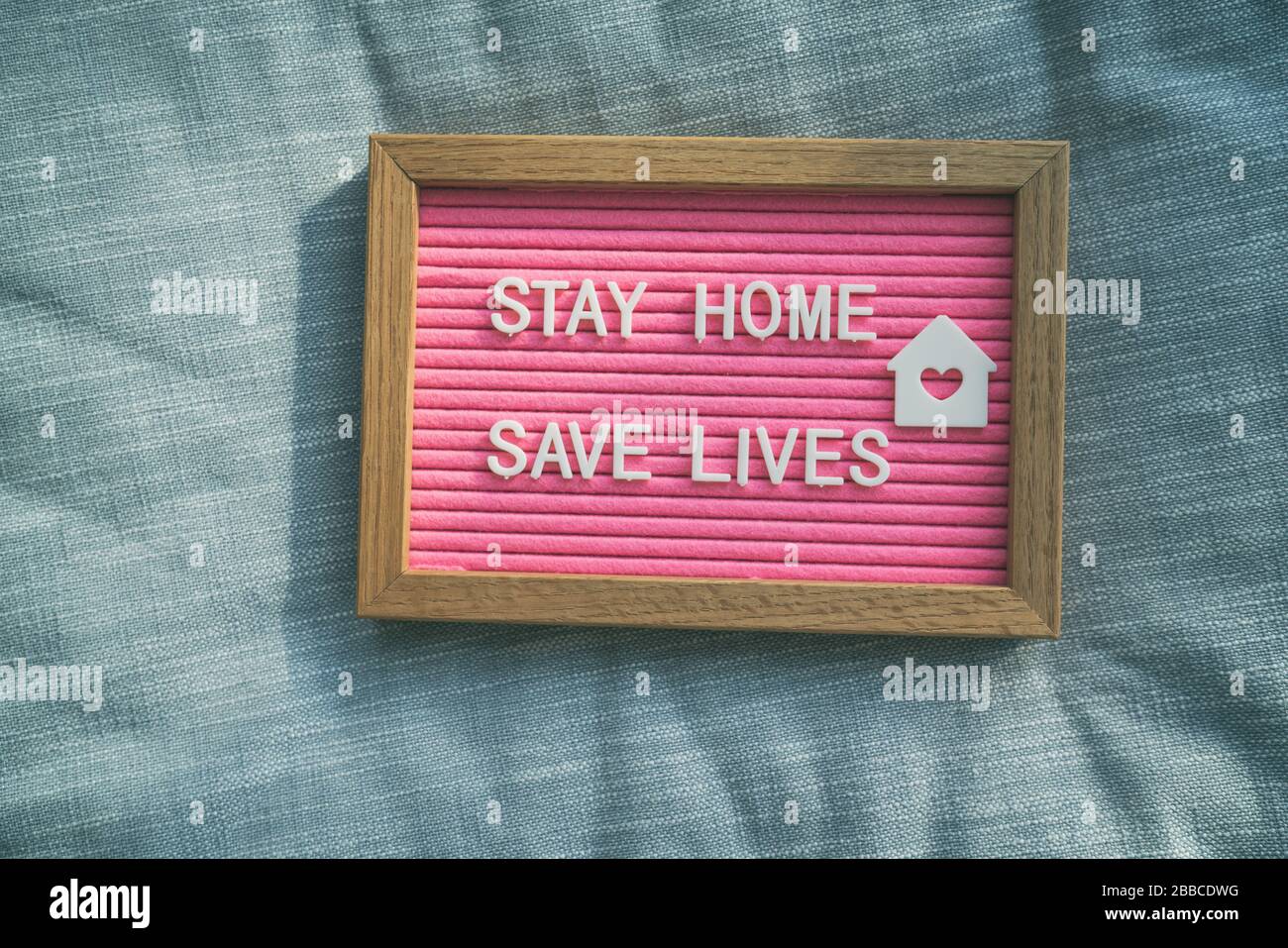 Coronavirus Angebot bleiben Sie zu Hause, retten Sie Leben rosafarbenes Filzbrettzeichen mit der Botschaft der Selbstisolierung für soziale Verantwortung auf dem Heimsofa-Hintergrund. COVID-19-Text zur Förderung des Aufenthalts zu Hause. Stockfoto
