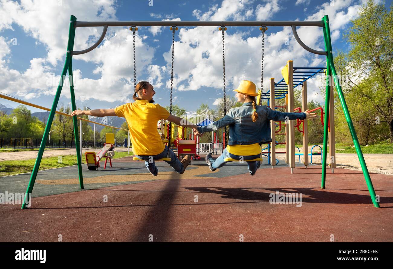 Glückliches Paar in blau und gelb Kleidung Fahrten bei Swing in Kinder Park in Almaty, Kasachstan Stockfoto