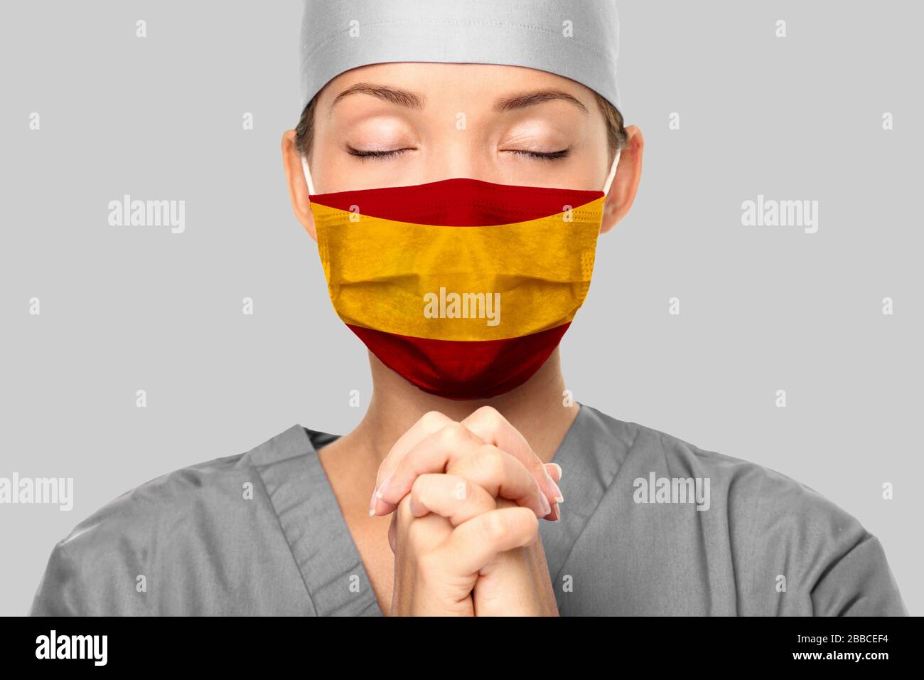 COVID-Ausbruch in Spanien asiatischer Arzt mit spanischem Flaggendruck auf der Operationsmaske, der um Hilfe betet. Junge Frau Krankenschwester betend. Coronavirus-Pandemie in Spanien. Stockfoto