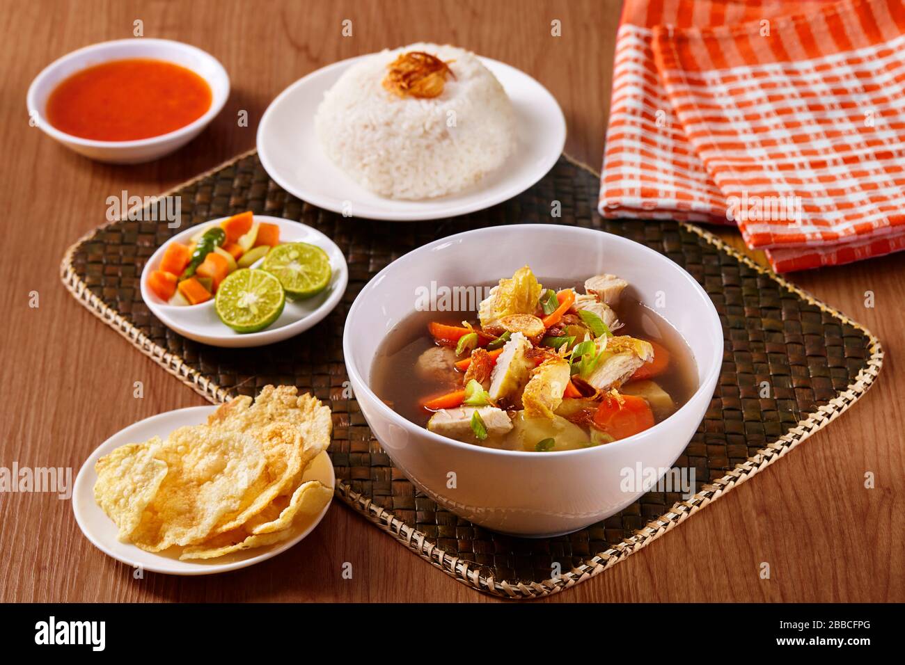 Traditionelle indonesische Hühnersuppe mit Reis, Gurken, Chips und Chilisauce Stockfoto